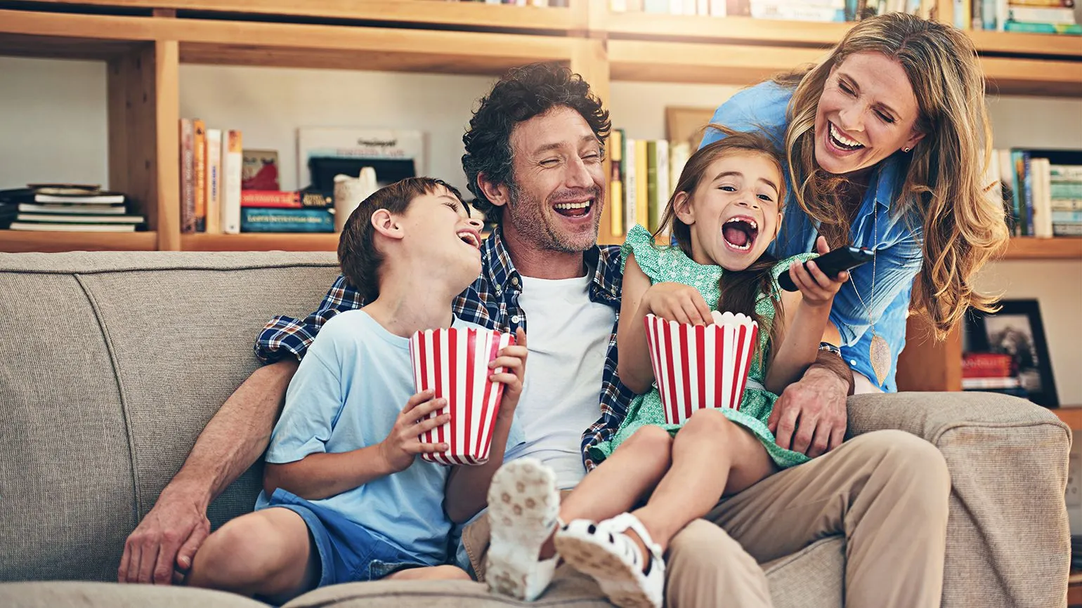 A happy family enjoying a movie night at home, sitting on a couch with popcorn, creating joyful memories together.